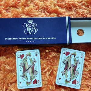 Puede incluir: Dos cartas de juego que representan a una reina con una corona y un corazón rojo sobre un fondo azul. El texto en las cartas dice "Collection Venise Simplon-Orient-Express Paris".