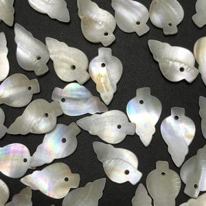 May include: Iridescent white shell pendants with a pearlescent sheen, scattered on a dark surface. The pendants have a variety of organic shapes, including leaf and teardrop designs, each with a small hole for stringing.