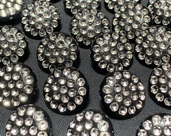 May include: Close-up of several black, round buttons with a multitude of small, clear, sparkling rhinestones. The buttons are arranged closely together, creating a textured, shimmering effect. The buttons are likely for sewing or crafting.