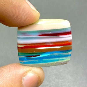 May include: A multi-colored glass cabochon with a layered design. The cabochon features stripes of red, orange, yellow, green, blue, and white.