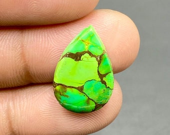 May include: A teardrop-shaped cabochon of green turquoise with brown matrix. The stone has a mottled green and brown pattern.