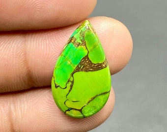 May include: A teardrop-shaped green turquoise cabochon with brown matrix inclusions. The stone has a bright green color and a smooth, polished surface.