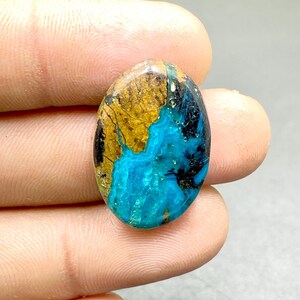 May include: Oval cabochon gemstone with a blue, green, and brown pattern. The stone has a smooth, polished surface.