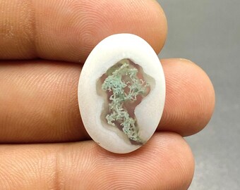Pode incluir: Gemstone cabochão oval com fundo branco e um padrão dendrítico verde no interior.