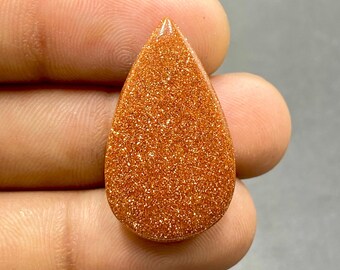 May include: A teardrop-shaped, orange-brown gemstone with a sparkly, glittery texture.