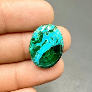May include: Oval cabochon gemstone with a green and blue pattern. The stone has a smooth, polished surface and is set in a bezel setting.