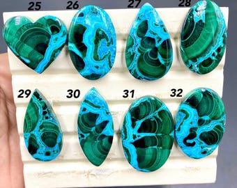Può includere: Una collezione di otto pietre preziose lucide di varie forme, tra cui un cuore, un ovale e una goccia. Le pietre presentano una sorprendente combinazione di tonalità verde intenso e blu vibrante, con motivi intricati. Le pietre preziose sono esposte su una superficie bianca.