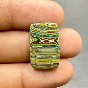 May include: A colorful, multi-layered agate cabochon with a rectangular shape. The stone features a variety of colors, including green, yellow, red, and white.