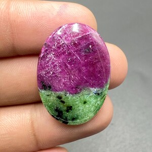 May include: Oval shaped green and pink gemstone cabochon with a smooth, polished surface. The gemstone has a layered appearance with a darker pink top and a lighter green bottom.