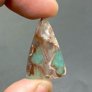 May include: A triangular shaped pendant made of green, brown, and white opal. The pendant has a smooth, polished surface.