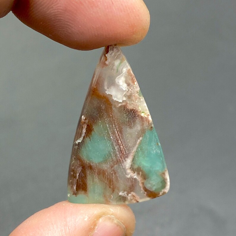 May include: A triangular shaped pendant made of green, brown, and white opal. The pendant has a smooth, polished surface.