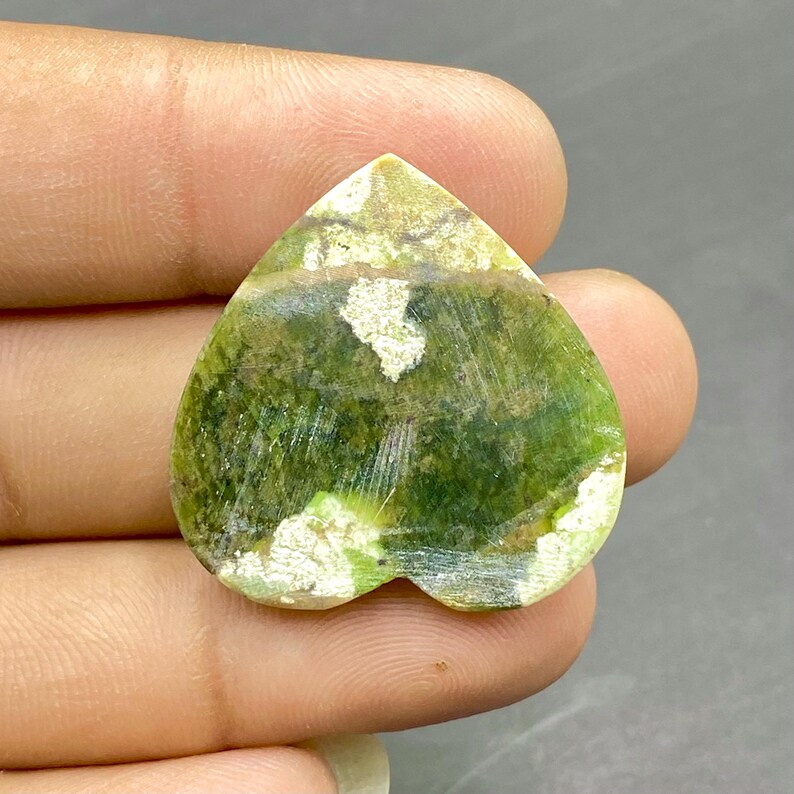 Op de afbeelding: Groen en wit hartvormig edelsteen met een gepolijste afwerking. De steen heeft een uniek patroon van groene en witte swirls.