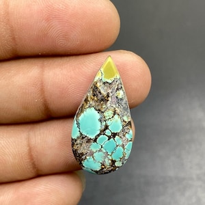 Peut inclure: Une pierre précieuse turquoise en forme de goutte d'eau présentant un mélange vibrant de sections bleu œuf de merle et jaune pâle, fortement entremêlées d'un motif matriciel brun foncé en forme de toile créant un aspect complexe et naturel.