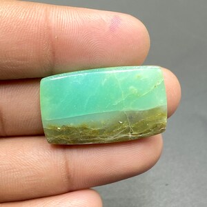 May include: A rectangular gemstone with a smooth, polished surface. The top half is a vibrant turquoise color, transitioning to a darker, olive-green hue at the bottom. The stone has natural veining and a slight crack.