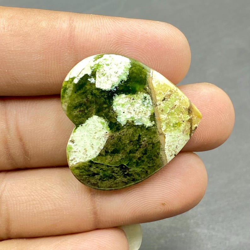 Op de afbeelding: Groen en wit hartvormige edelsteen cabochon met een gevlekt patroon.