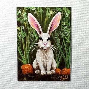 May include: An oil painting on canvas featuring a white rabbit with long ears, pink nose, and dark eyelashes, sitting in a garden. The rabbit is surrounded by green carrot tops and orange carrots planted in dark soil. The artist's signature is in the corner.