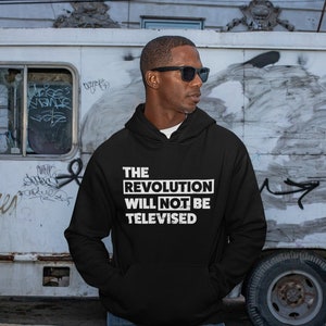 May include: A black hooded sweatshirt with the text "THE REVOLUTION WILL NOT BE TELEVISED" in white letters.