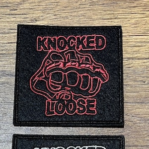 Può includere: Due toppe quadrate nere con cuciture bianche. La toppa superiore ha cuciture rosse e il testo "KNOCKED LOOSE" in bianco. La toppa inferiore ha cuciture bianche e il testo "KNOCKED LOOSE" in nero.