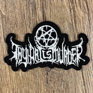 May include: Black embroidered patch with the text "Thy Art Is Murder" in a gothic font. The patch features a white pentagram design above the text. The patch is rectangular with a decorative border.