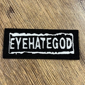 Peut inclure: Écusson rectangulaire noir avec le texte blanc « EYEHATEGOD » bordé d'un contour blanc vieilli. Ce patch est destiné à être appliqué sur des vêtements ou des accessoires.