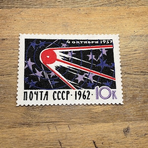 Puede incluir: Un sello postal soviético vintage con una ilustración roja y blanca de un satélite orbitando la Tierra. El sello es blanco y negro con una denominación de "10K" en morado y el texto "ПОЧТА СССР - 1962" en escritura cirílica. El sello también incluye el texto "4 ОКТЯБРЯ 1957" en escritura cirílica.