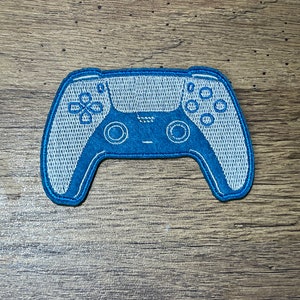 Può includere: Una toppa ricamata blu e bianca di un controller per videogiochi.