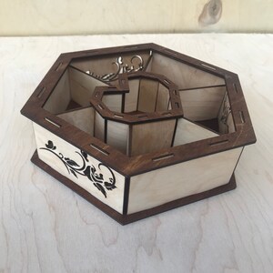 May include: A hexagonal wooden box with a decorative floral design. The box has multiple compartments and is made of light and dark wood.