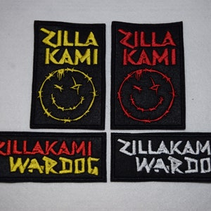 Peut inclure: Quatre patchs brodés avec le texte "ZillaKami" en différentes couleurs. Deux patchs présentent un smiley en fil de fer barbelé, l'un en jaune et l'autre en rouge. Les deux autres patchs présentent le texte "ZillaKami Wardog", l'un en jaune et l'autre en blanc.