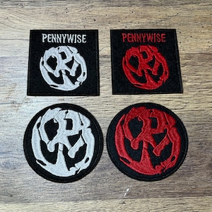 Op de afbeelding: Vier geborduurde patches met het Pennywise-logo. Twee patches hebben een zwarte achtergrond met een wit logo, en twee patches hebben een zwarte achtergrond met een rood logo.