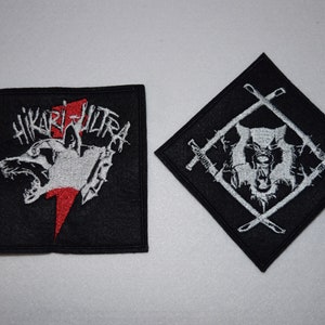 Peut inclure: Deux patchs brodés noirs avec des coutures blanches et rouges. Le premier patch représente une tête de loup avec le texte "Hikari Ultra" au-dessus. Le deuxième patch représente une tête de loup à l'intérieur d'un losange avec deux épées croisées.