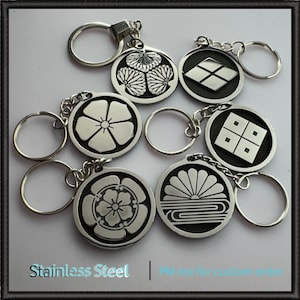 Puede incluir: Llaveros de acero inoxidable con varios diseños de escudos de armas japoneses. Cada llavero presenta un colgante circular con patrones intrincados y un llavero plateado. El texto "Stainless Steel" es visible en la parte inferior.