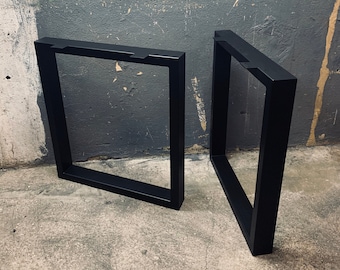 Könnte beinhalten: Zwei schwarze Metalltischbeine mit quadratischem Rahmen. Die Beine sind abgewinkelt und auf einem Betonboden platziert.