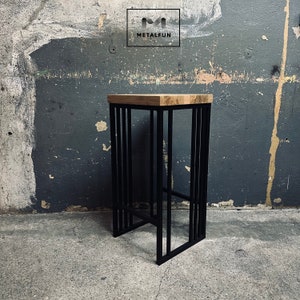 Op de afbeelding: Een moderne barkruk met een licht houten zitting en een zwart metalen frame. Het frame heeft verticale staven en een voetsteun. Het logo "METALFUN" is zichtbaar.