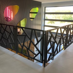 May include: A modern staircase with a black metal railing featuring a geometric design. The wall behind the railing is dark with vertical lines, and there are colorful, abstract wall decorations. A large window provides natural light.