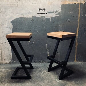 May include: Two modern bar stools with a black metal frame and a light-colored wooden seat. The frame has a unique Z-shaped design. The stools are displayed against a textured gray wall. The logo "METALFUN" is visible in the background.