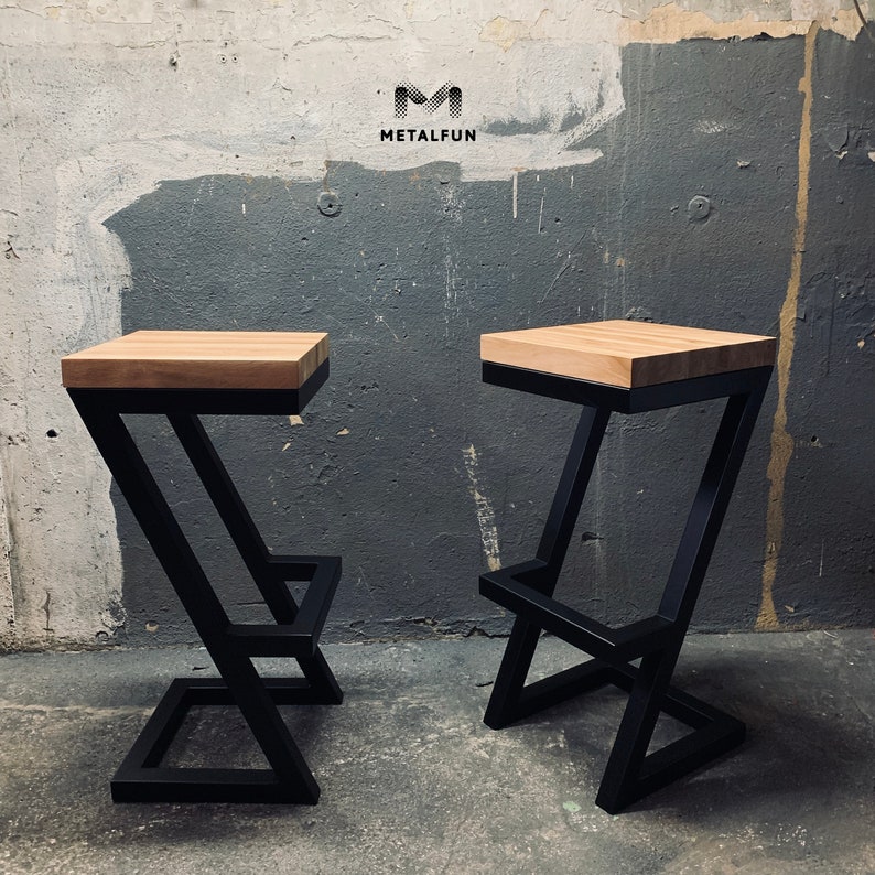 May include: Two modern bar stools with a black metal frame and a light-colored wooden seat. The frame has a unique Z-shaped design. The stools are displayed against a textured gray wall. The logo "METALFUN" is visible in the background.
