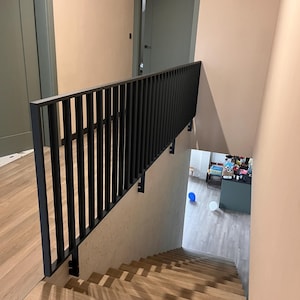Könnte beinhalten: Eine moderne Treppe mit Holzstufen und einem schwarzen Metallgeländer. Die Wände sind in einem hellen Pfirsichton gestrichen, und eine graue Tür ist oben auf der Treppe zu sehen. Der Boden ist aus hellem Holz.