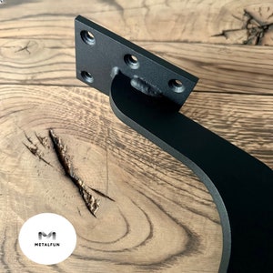 May include: Black metal bracket with a curved arm and a rectangular mounting plate. The bracket has four holes for mounting.