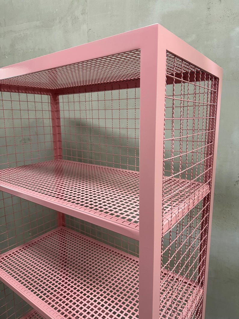 May include: A pink metal shelving unit with three shelves. The shelves and sides are made of a wire mesh. The frame is a solid pink color. The unit is designed for storage and display.