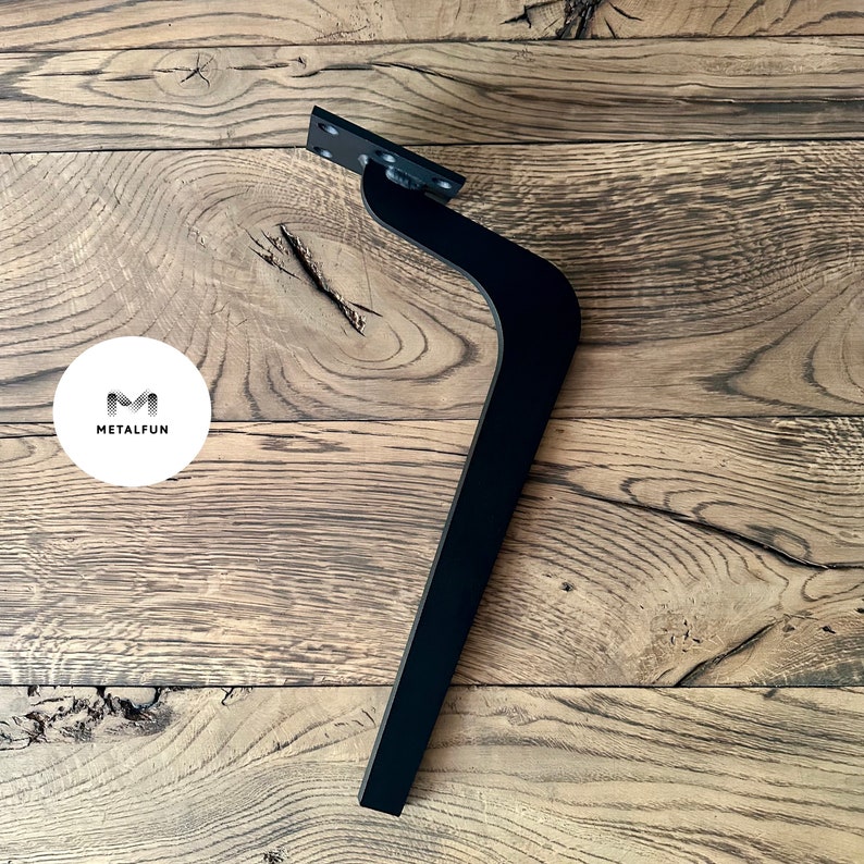 May include: Black metal furniture leg with a curved design. The leg is mounted on a wooden surface.