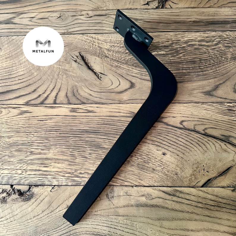 May include: Black metal furniture leg with a curved design and a square mounting plate. The leg is shown on a wooden surface.