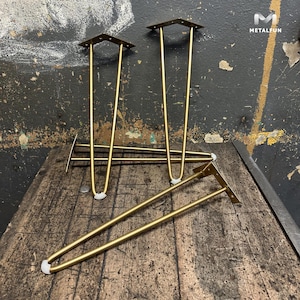 Op de afbeelding: Vier gouden metalen haarspeldpoten met witte kunststof voetjes. De poten zijn op een houten oppervlak gerangschikt.