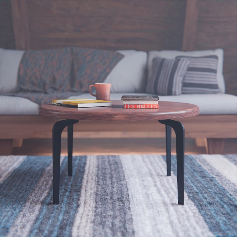 May include: A wooden coffee table with black metal legs. The table is round and has a natural wood finish. There are three books and a red mug on the table.