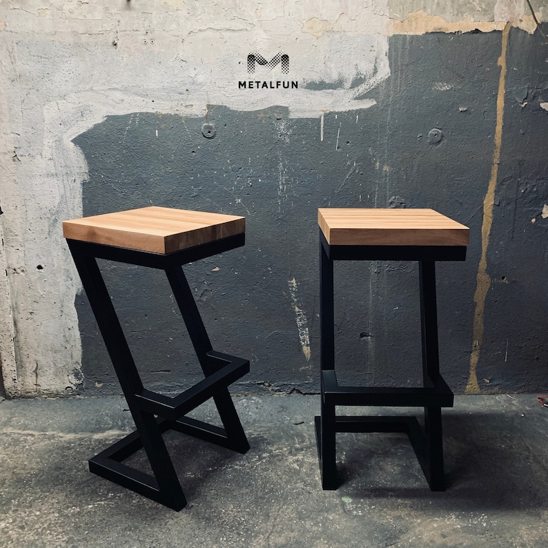 May include: Two modern bar stools with a light wood seat and black metal frame. The stools have a minimalist design, one with a Z-shaped leg and the other with a square leg. The logo "METALFUN" is visible in the upper left corner.