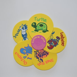 May include: A yellow bath toy set with a flower shape. Each petal features a different sea creature, including a turtle, squid, lobster, octopus, and shell fish. The center of the flower has a pink circle with the text "Bathtime Book".