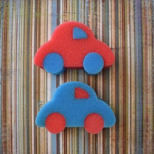 May include: Two toy cars made of sponge, one red and one blue, with a striped background.