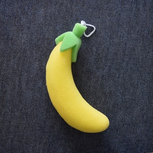 May include: A yellow sponge banana bath scrubber with a green leaf on top. The banana has a white string loop for hanging.
