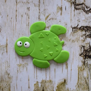 May include: A green rubber turtle toy with a smiling face and a textured shell. The turtle has two large eyes and a small mouth.
