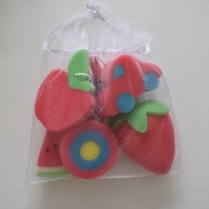 May include: A set of six colorful bath sponges shaped like fruit, including a watermelon, apple, strawberry, and a target-shaped sponge. The sponges are packaged in a white mesh bag.