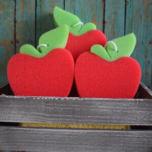 May include: Three red sponge apples with green leaves in a gray wooden crate. The crate is sitting on a blue and green wooden surface.